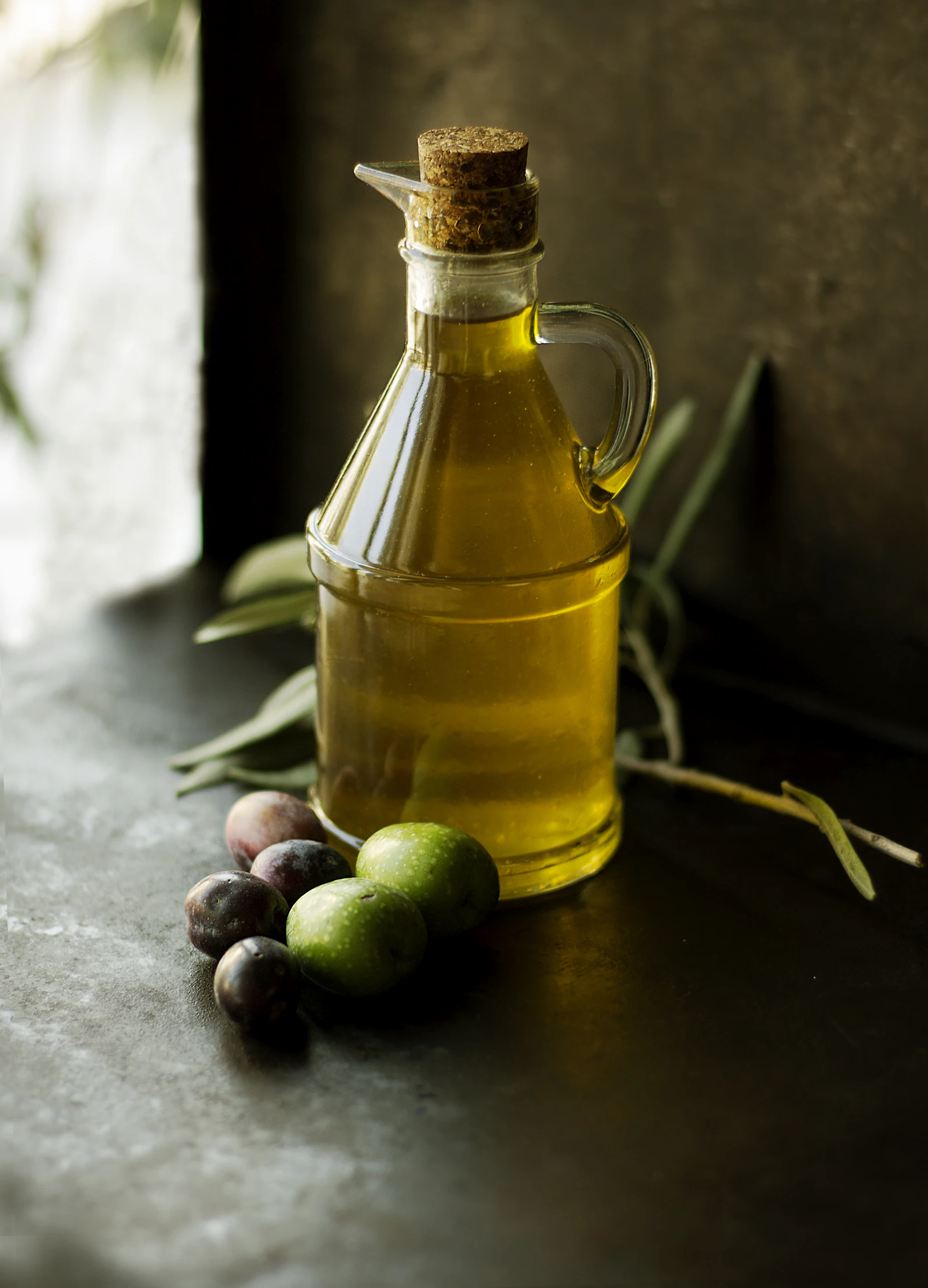 A glass bottle of extra virgin olive oil with fresh olives